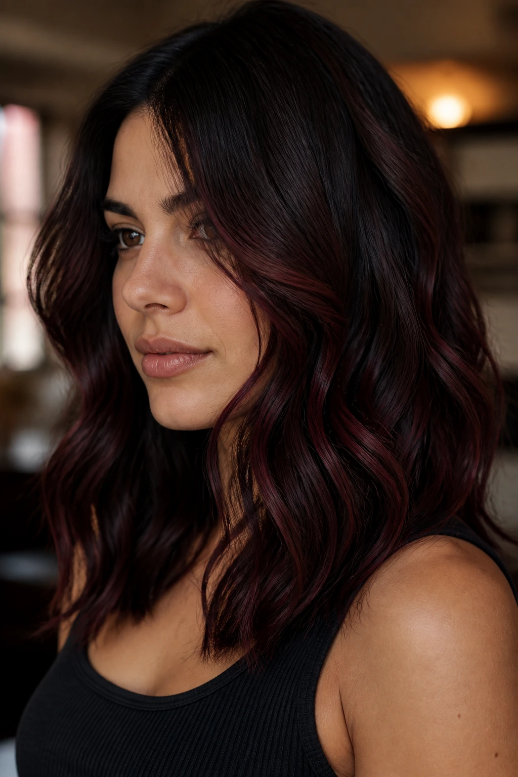 Close-up of a woman with burgundy balayage on deep brown, wavy hair.