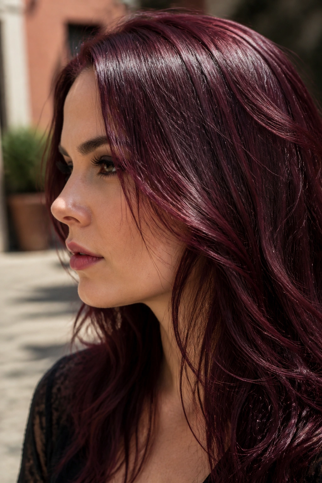 Close-up portrait of a person with burgundy wine hair in a sunlit courtyard
