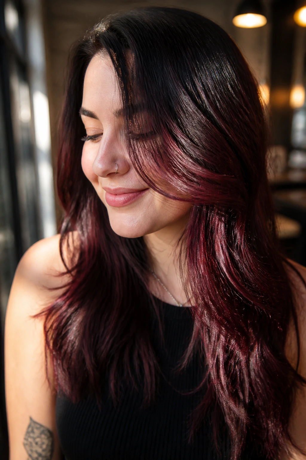 Close-up portrait of a real person with cherry cola deep red peekaboo hair under warm cafe light