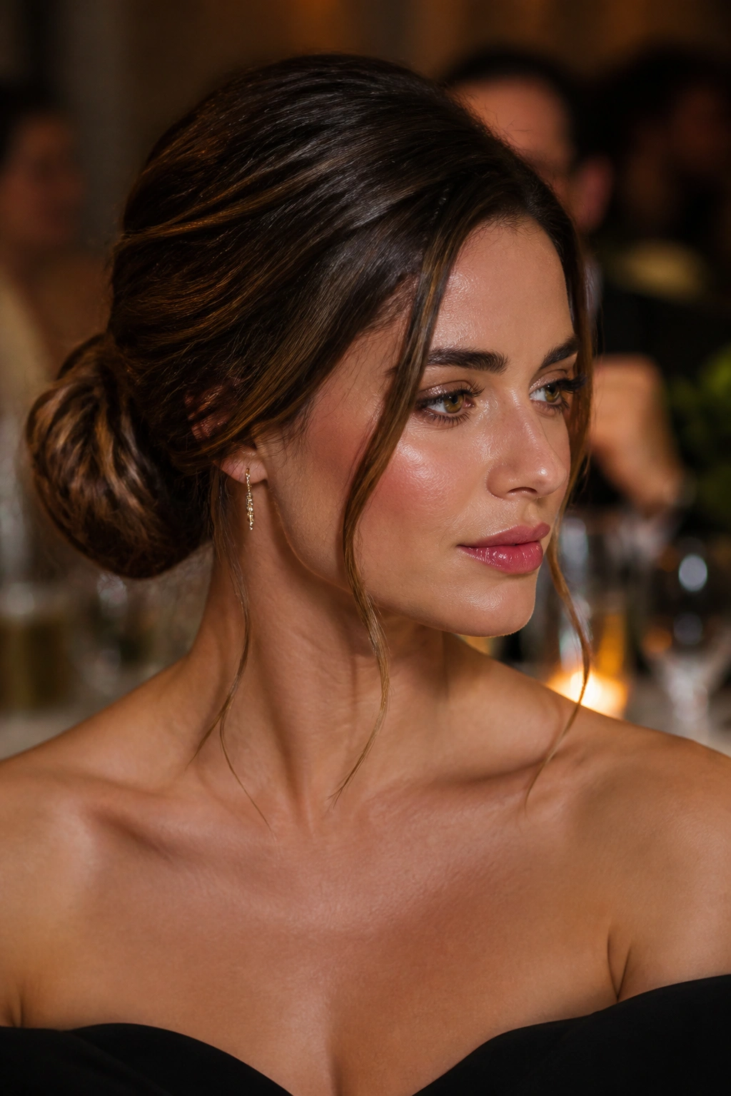 Close-up of a woman with side-part chignon and face-framing tendrils in warm event lighting.