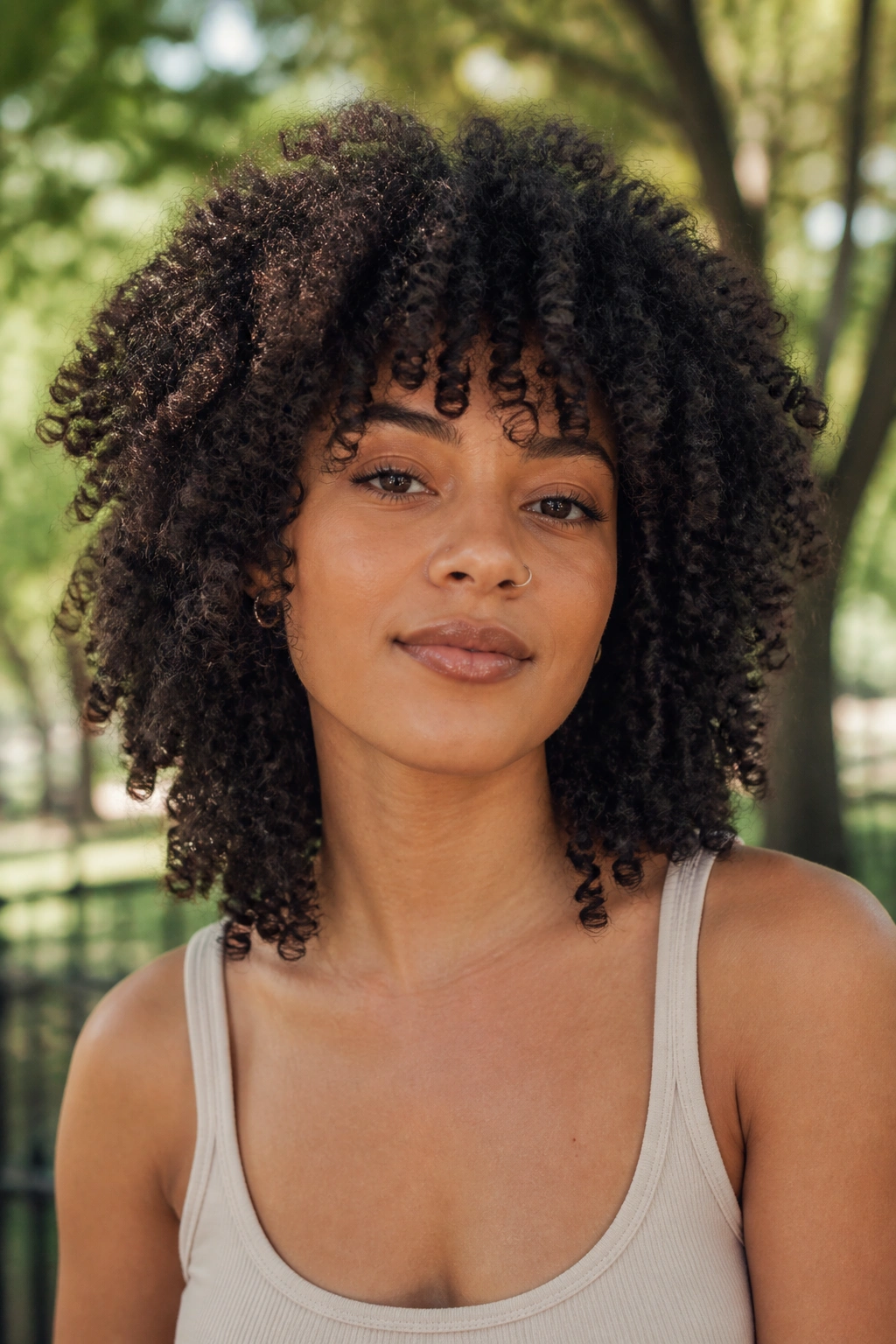 Close-up of a real woman with natural coils forming a rounded wolf cut in park sunlight