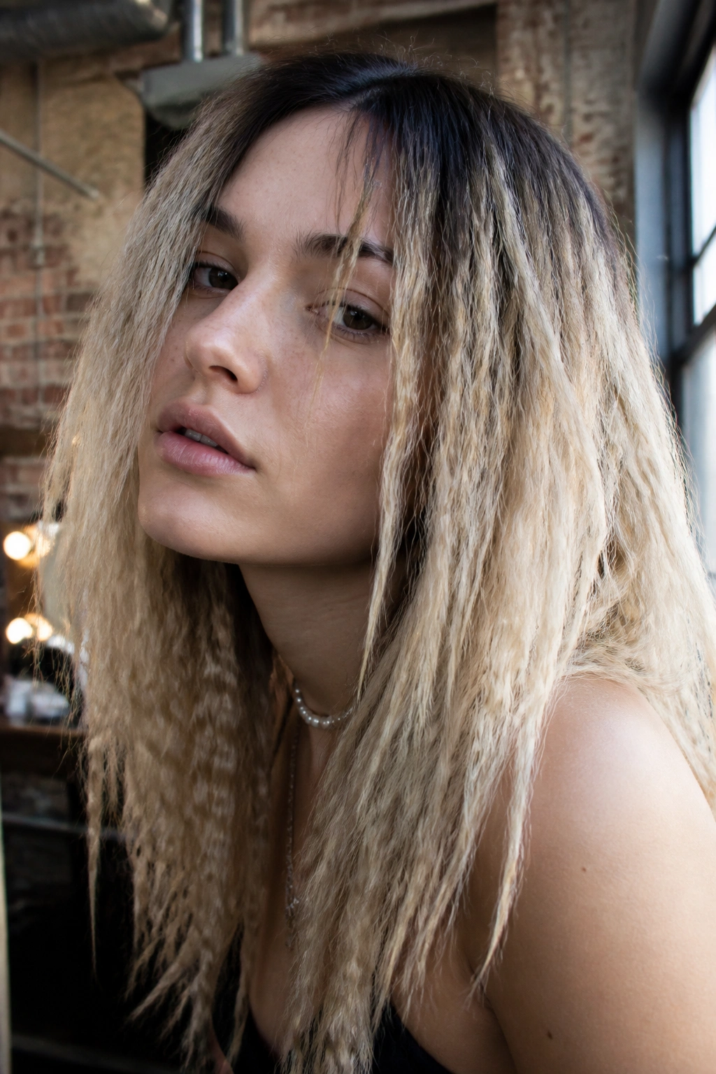 Close-up portrait of a real person with crimped hair and dark roots, gritty texture and face-framing pieces
