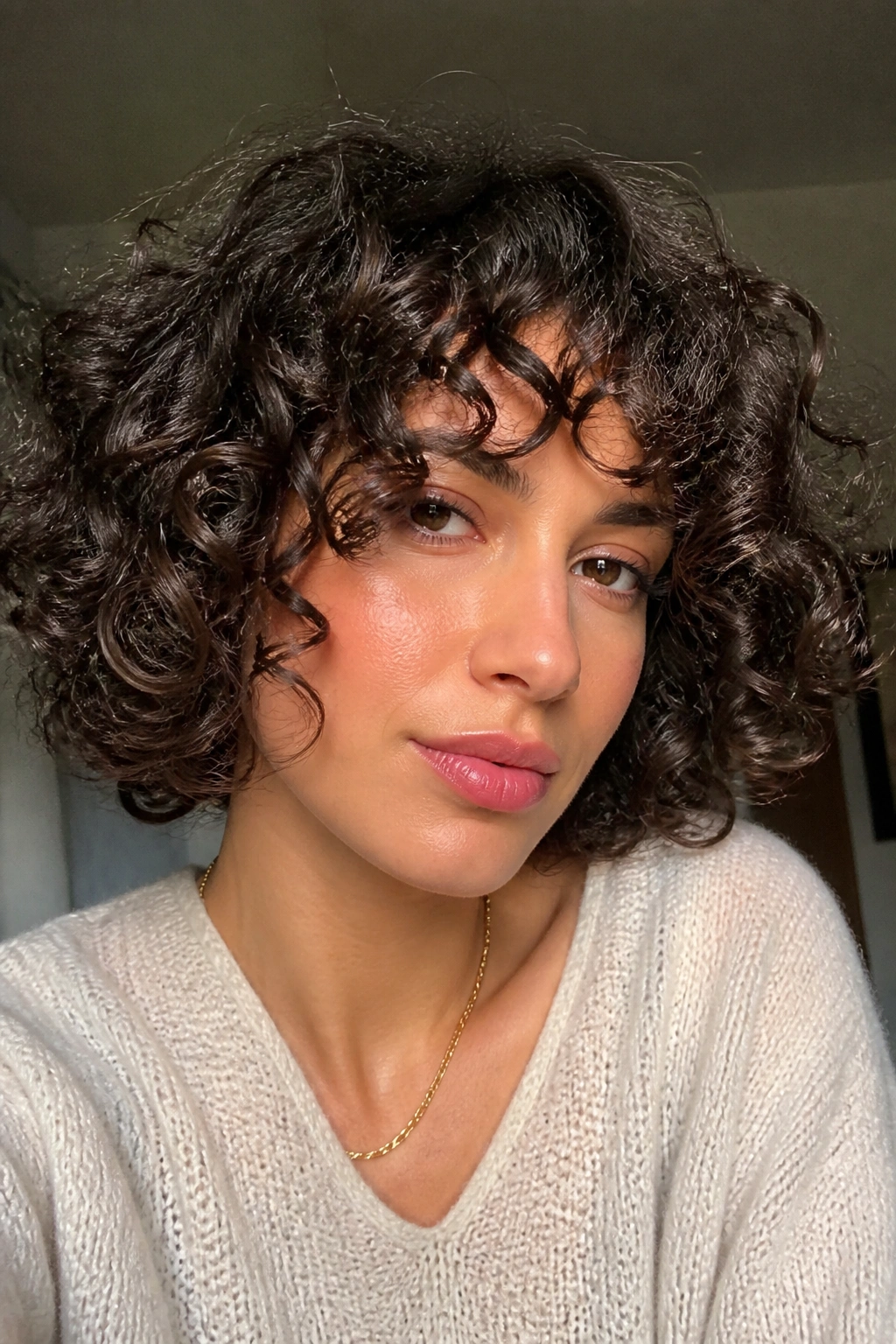 Portrait of a woman with curly bob and bangs in warm indoor light