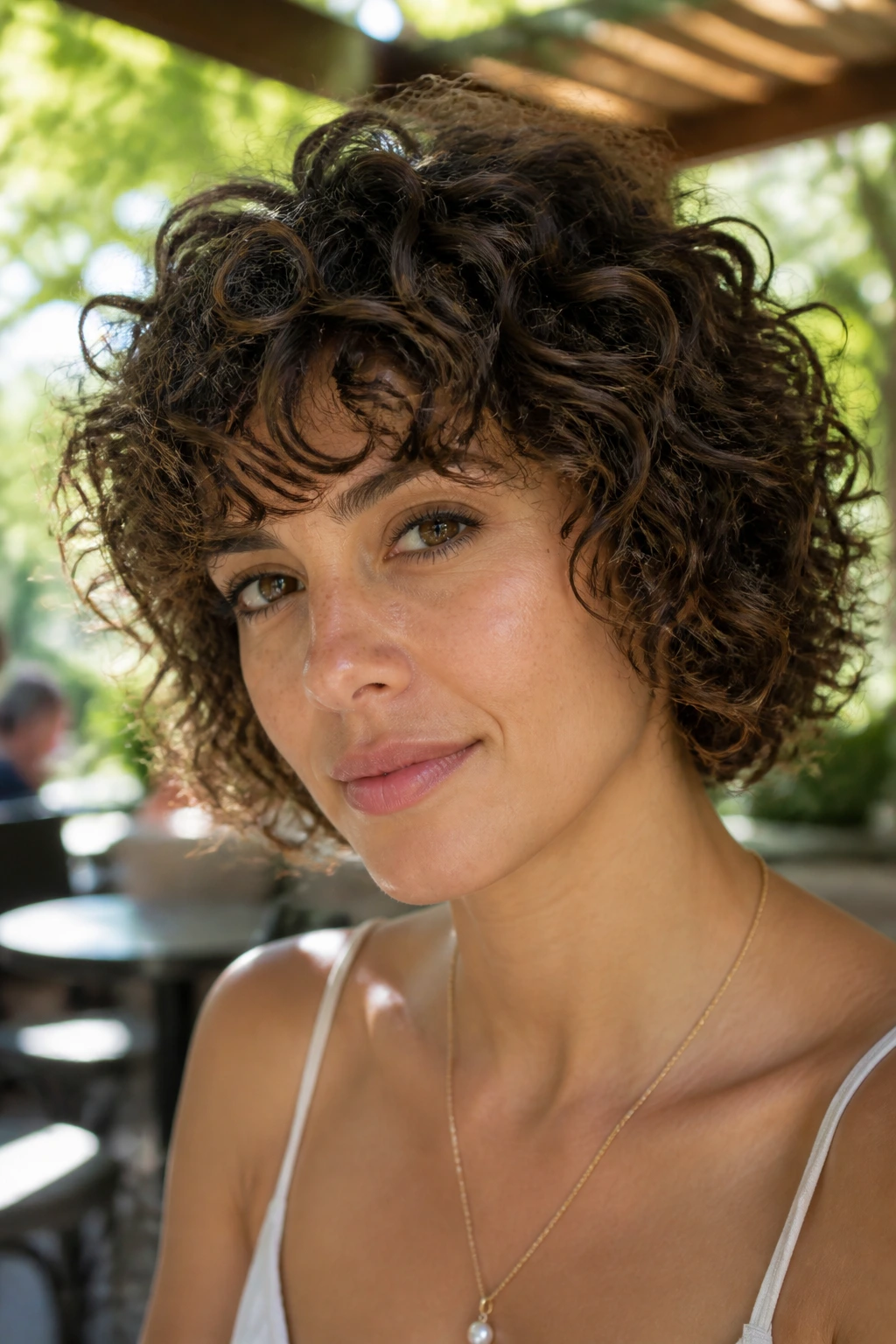 Close-up of a woman with curly layered bob in outdoor cafe daylight