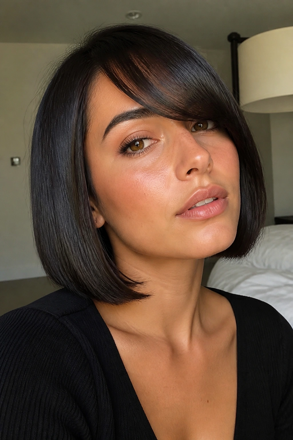 Close-up of a real woman with a glassy sleek bob and side-swept fringe in a modern bedroom