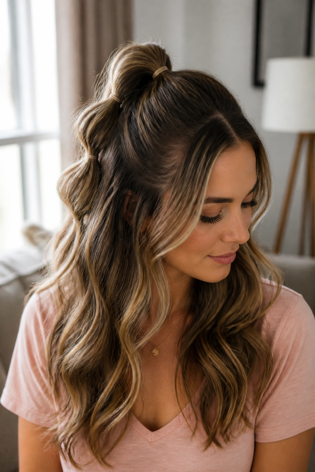 Close-up of a real woman with a half-up bubble ponytail on loose waves in soft window light.