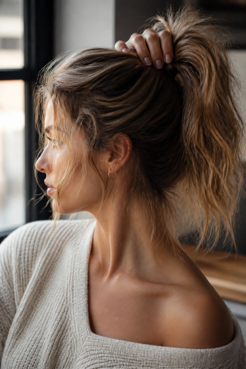 Close-up of a woman with a messy textured ponytail and loose face-framing strands.