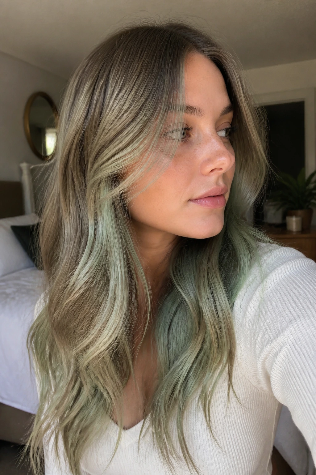 Close-up of a real woman with muted sage peekaboo hair color in soft window light
