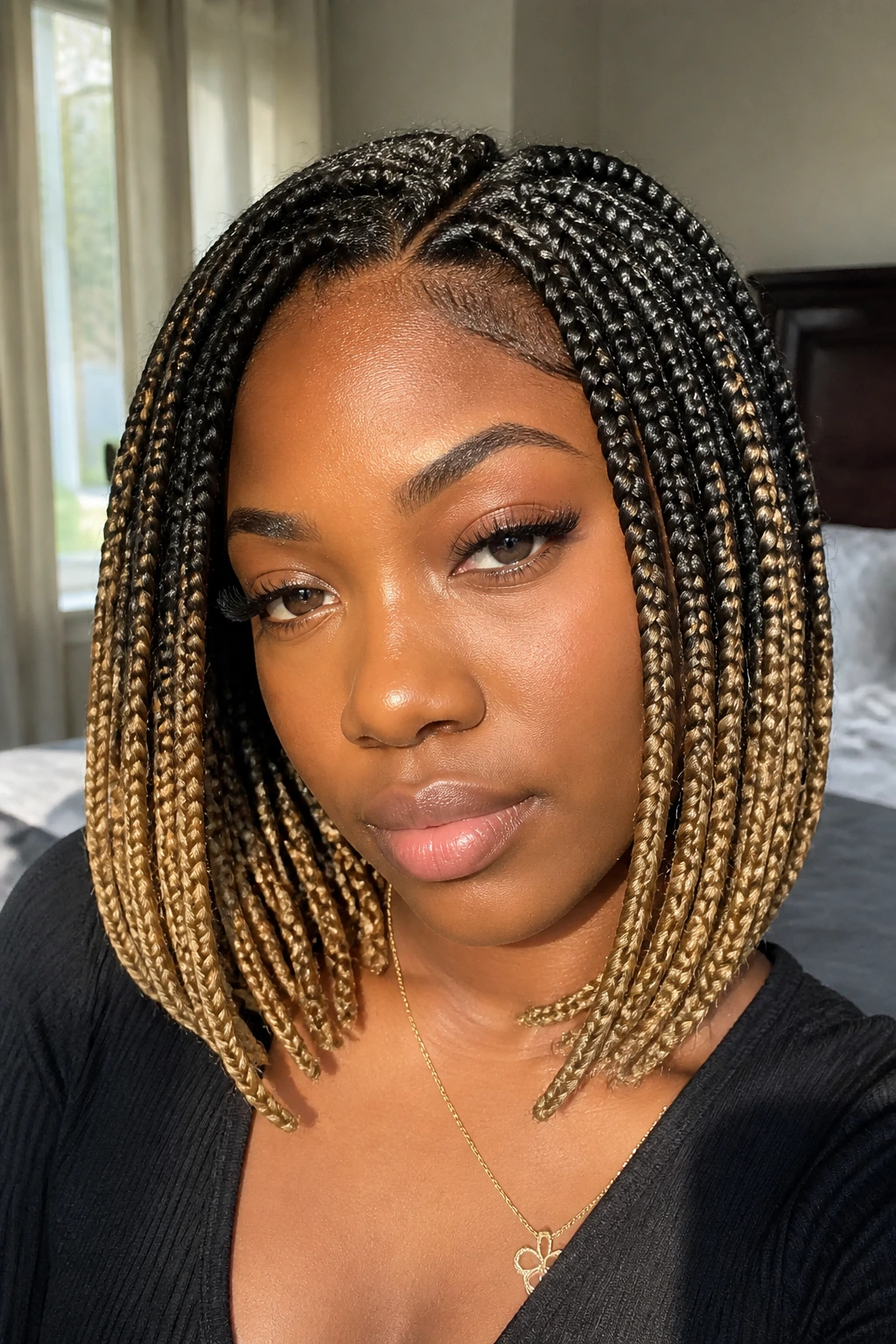 Close-up of a real woman with a colored ombré braided bob, from dark roots to lighter ends, by a sunlit window