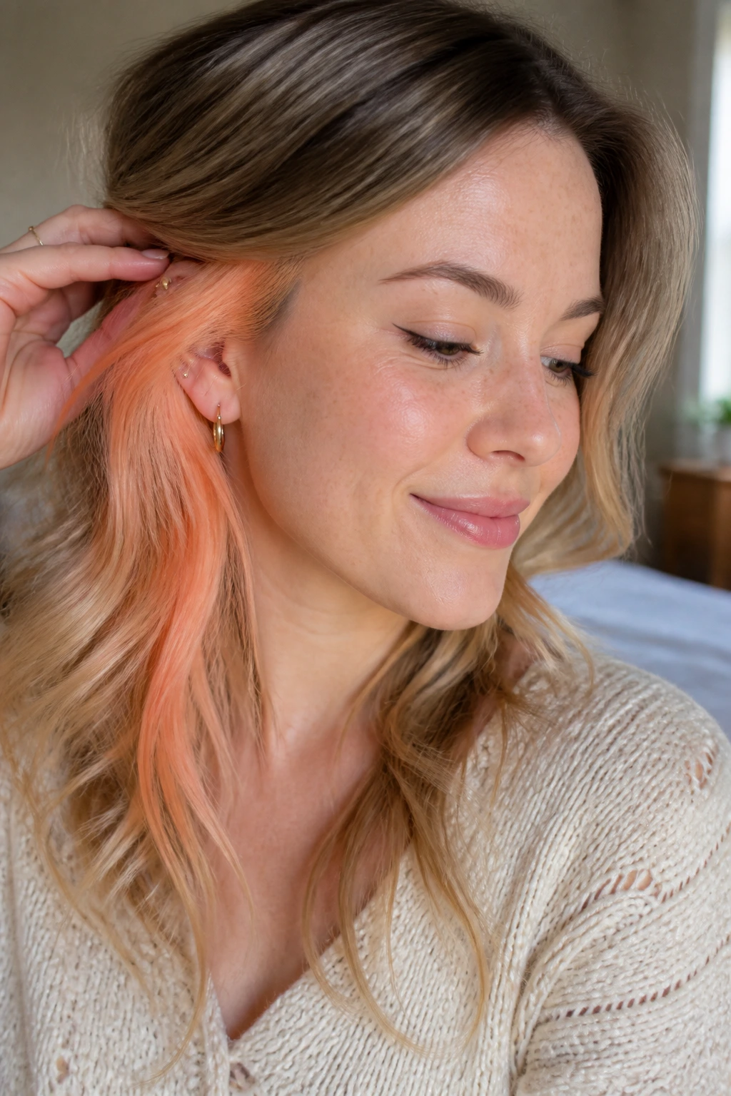 Close-up of a real woman showing a peach apricot peekaboo hair color near the temple.