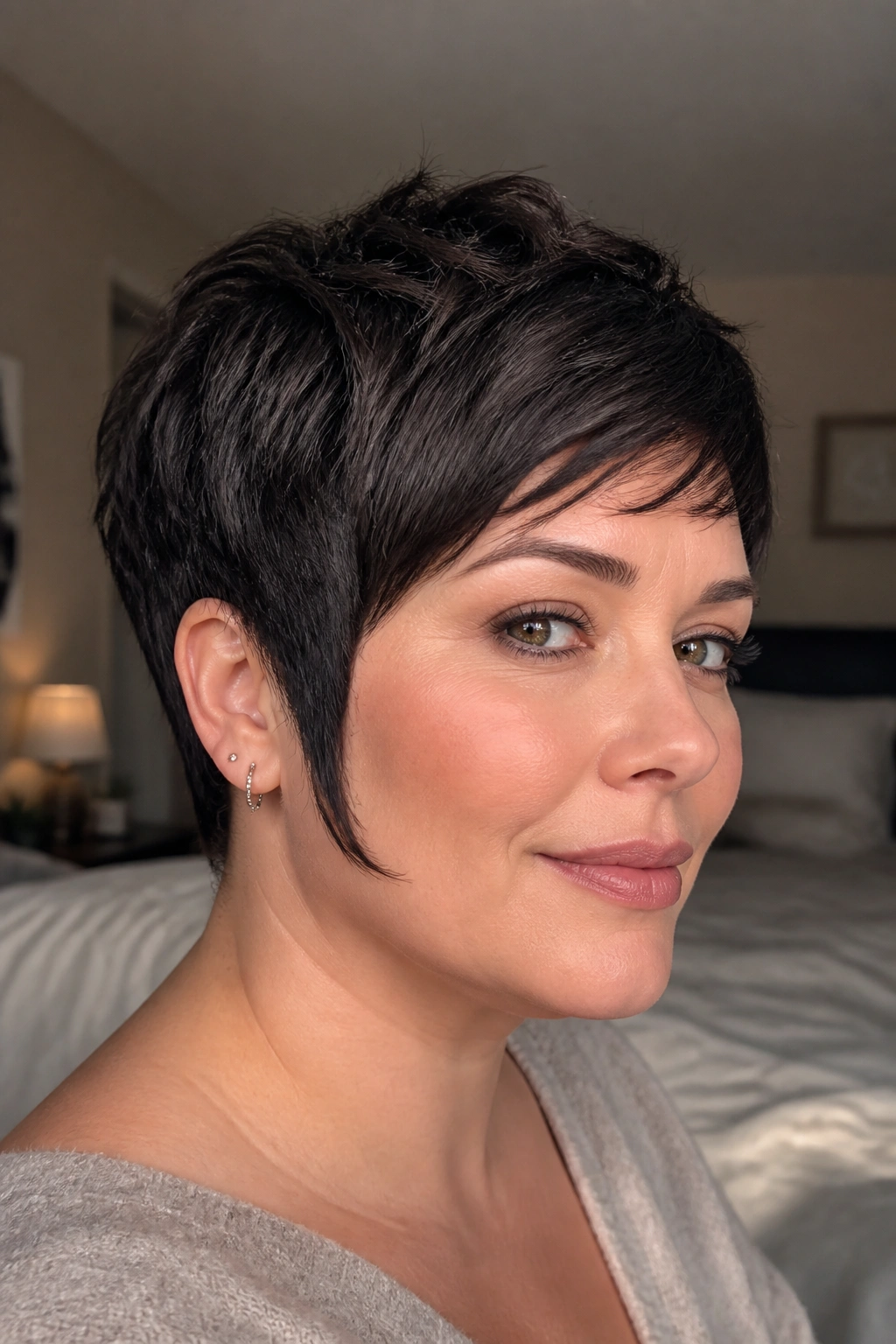 Close-up of a real woman with a face-framing sideburn pixie hairstyle in warm bedroom light