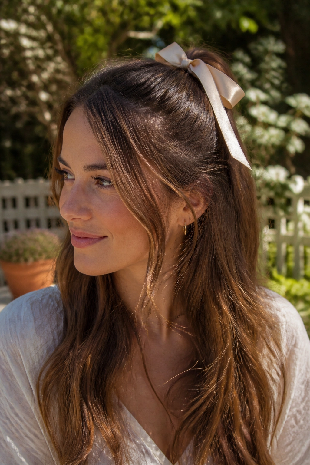 Close-up portrait of a real woman with ribbon-tied half up hairstyle on a sunlit patio.