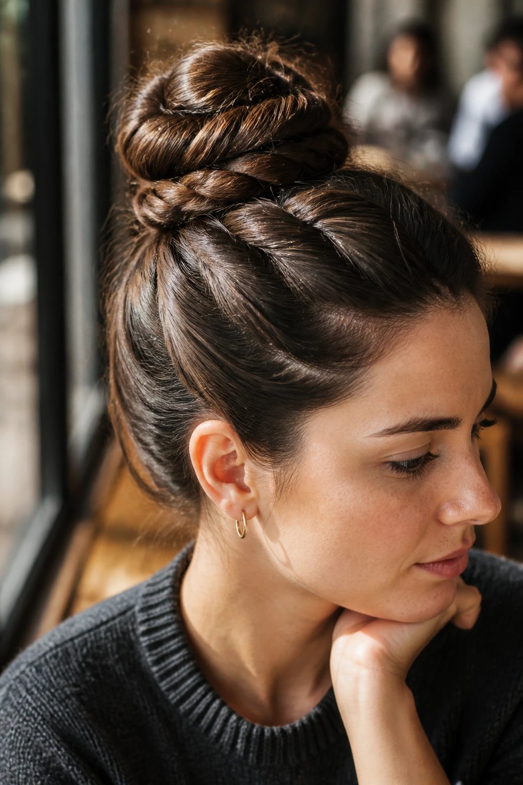 Close-up of a real woman with a rope bun at the crown in a sunlit cafe setting