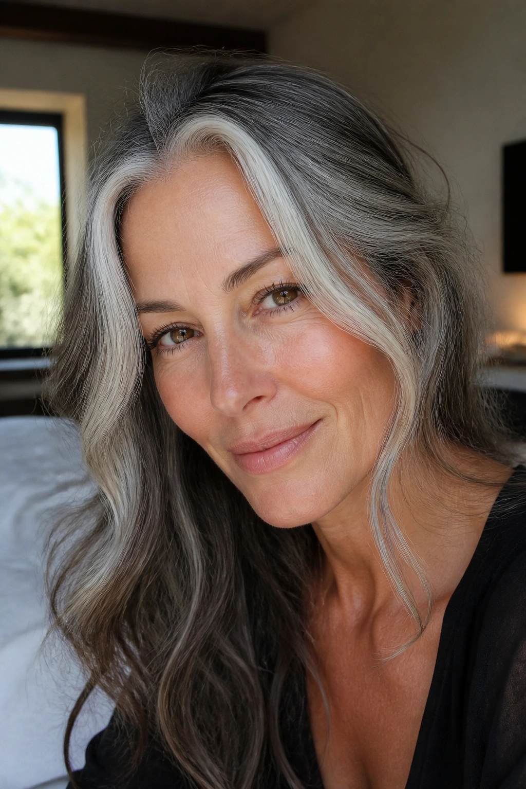 Close-up of a real woman with face-framing silver ribbons in salt-and-pepper hair, natural window light