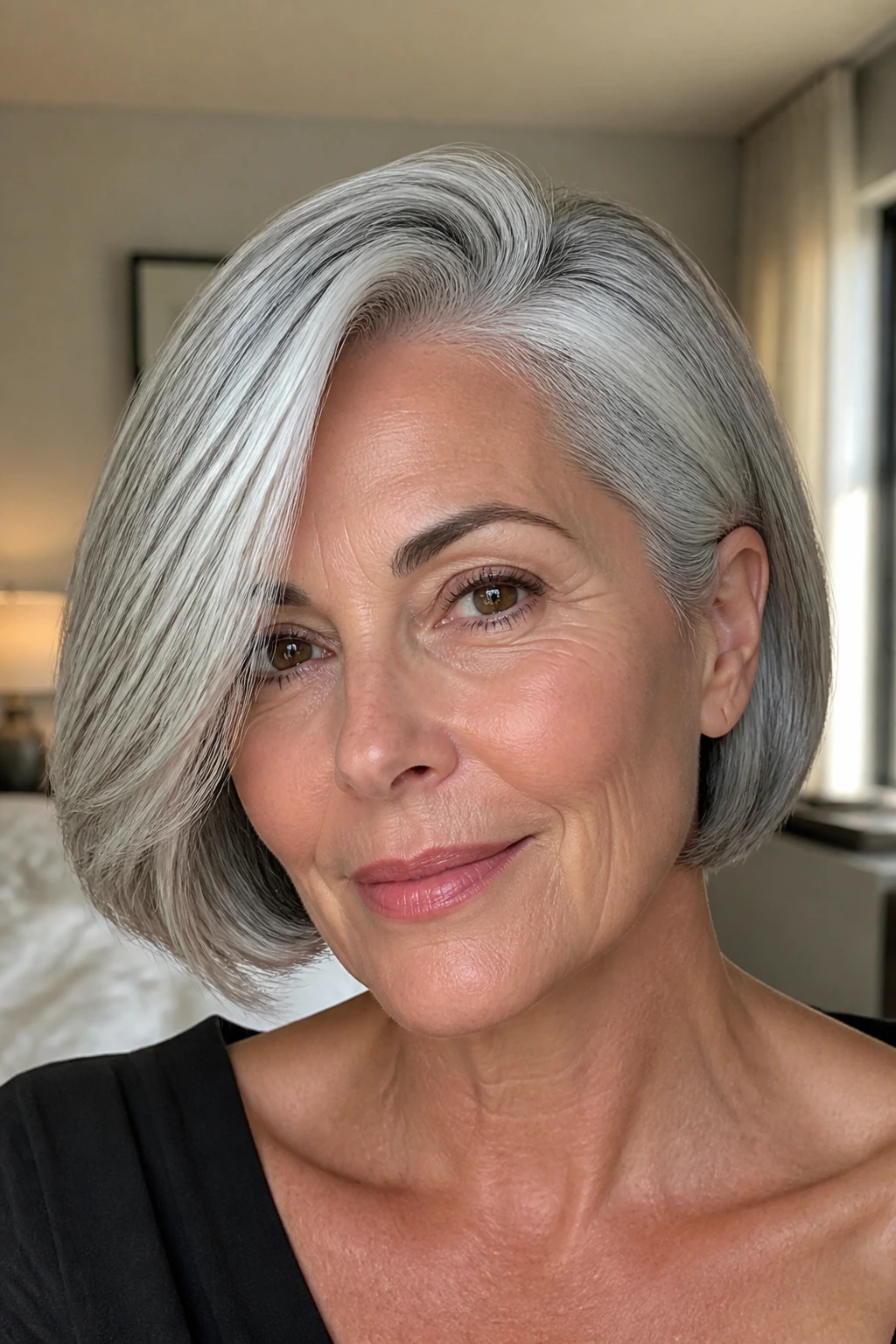Close-up portrait of a real woman with a side-part bob and gray hair in natural window light.