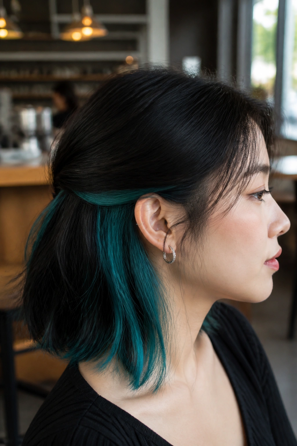 Close-up of a real woman showing teal peekaboo chunks under dark hair layers