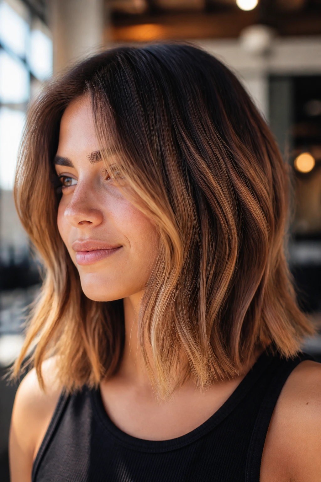 Close-up of a real woman with a shoulder-length lob featuring toasted caramel highlights in a sunlit setting