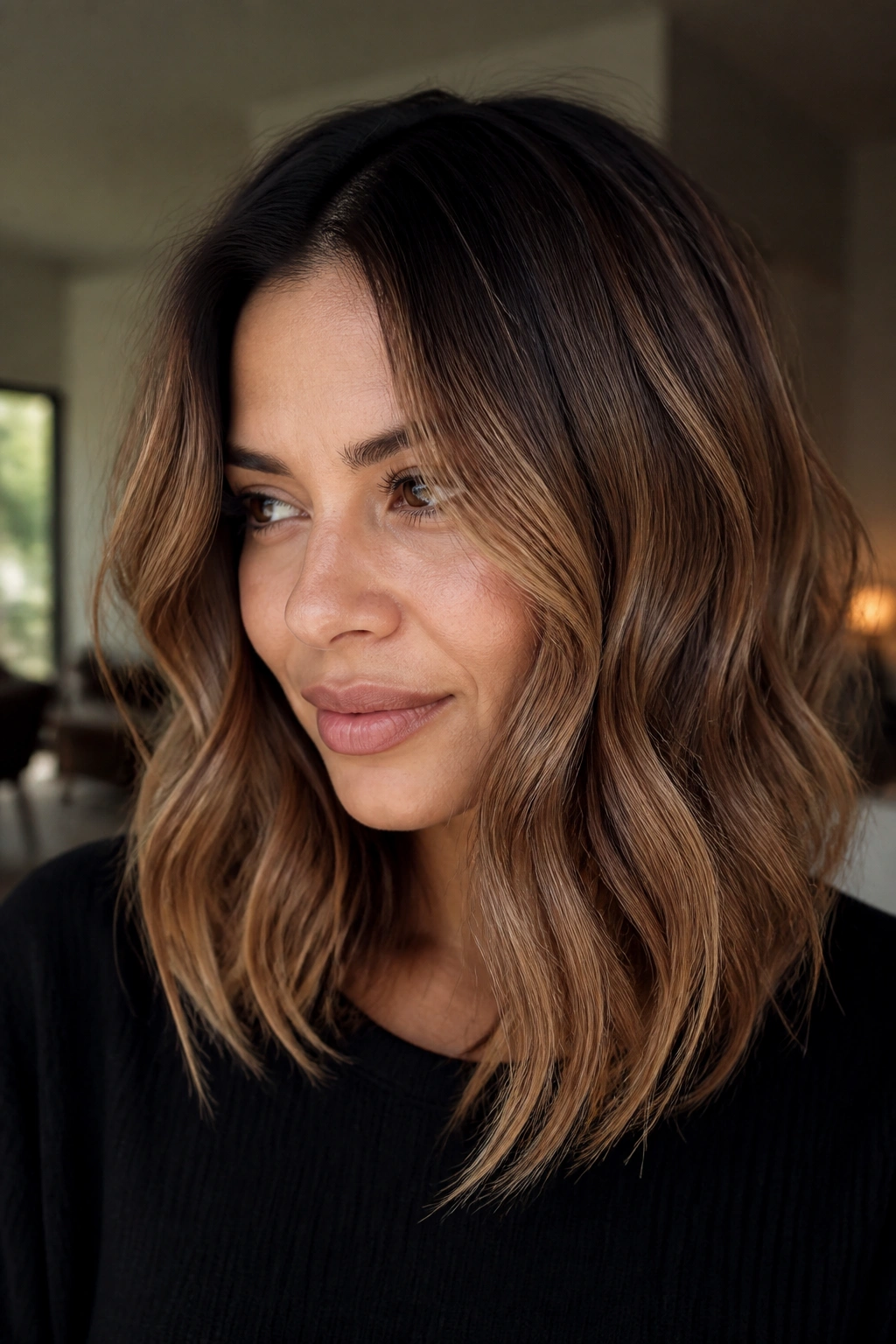 Close-up portrait of a woman with toffee brown hair and a shadow root in warm window light