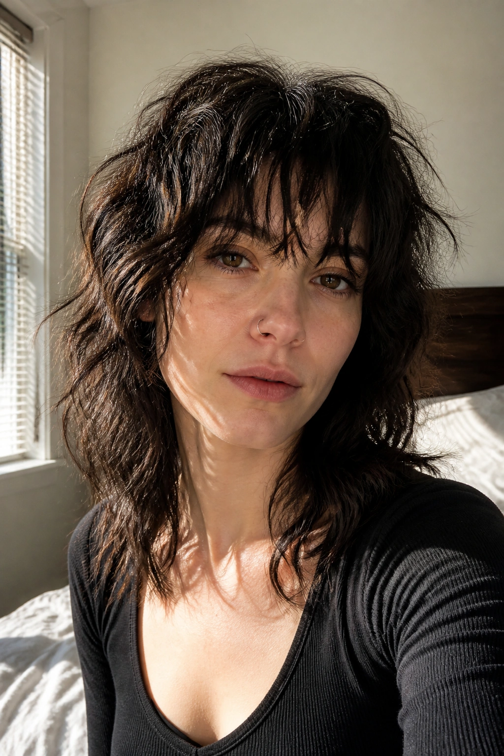 Close-up of a real woman with a wavy bedhead wolf cut in a sunlit bedroom