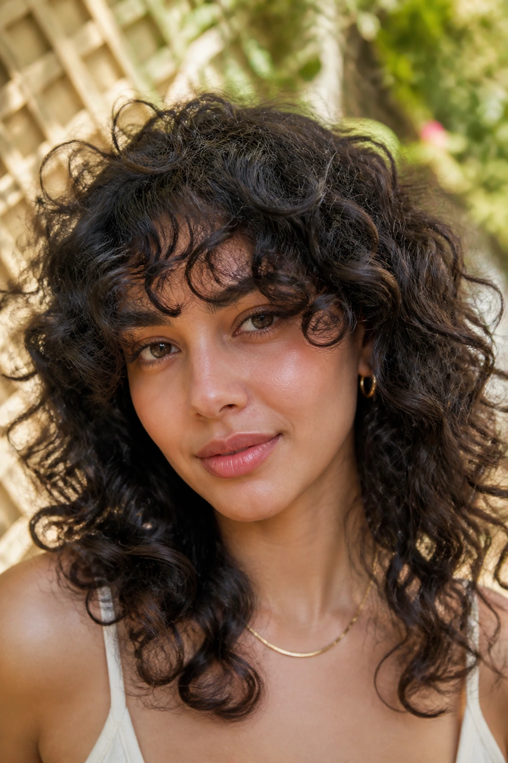 Close-up of a real woman with curly curtain bangs framed by natural curls in soft sunlight